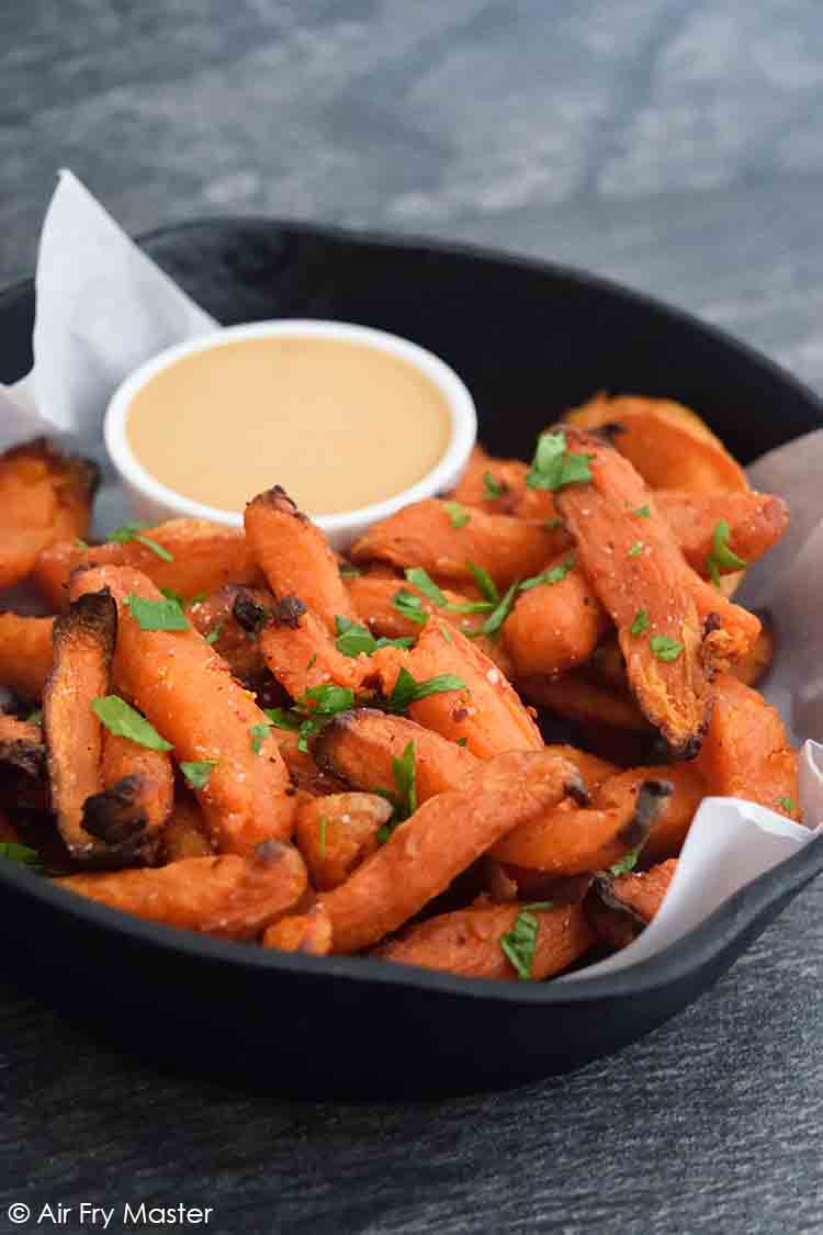 A midline view of a cast iron skillet filled with Air Fryer Sweet Potato Fries and a side dish of fry dip.