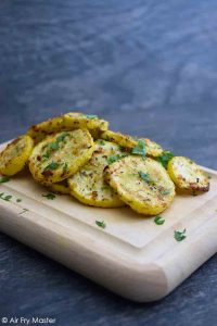 A side view of a pile of Air Fryer Yellow Squash on a cutting board, topped with fresh, chopped parsley.