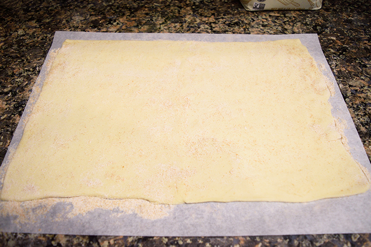 Puff pastry rolled out on a piece of floured parchment paper in preparation for making Air Fryer Pizza Rolls.