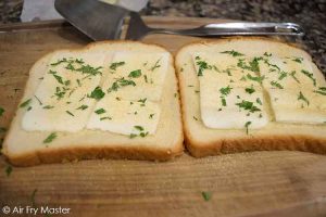 The two bread slices topped with butter, garlic powder and chopped parsley.