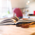 An up close shot of two wooden spoons next to an open cookbook laying on a countertop.