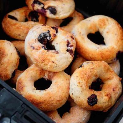 A stack of Air Fryer Bagels With Blueberries sit in a black air fryer basket.