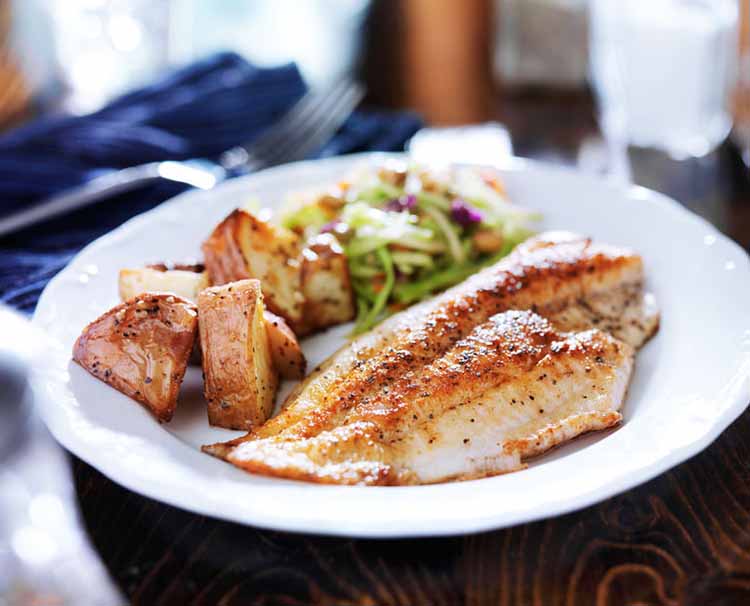 Fillet of fish with some roasted potato wedges and vegetables.