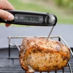 An Instant Read Thermometer takes the temperature of a piece of pork sitting on a rack.