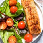 Air fryer salmon sits on a plate with a green salad.