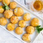 Keto air fryer caramel goat cheese balls sit lined up on a platter with some fresh greens between them for garnish.