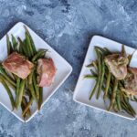 Air Fryer Pesto Chicken on two serving plates atop a bed of asparagus on each plate. One of many recipes in this guide to the best keto air fryer recipes.