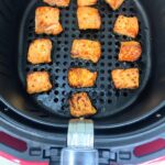 Three rows of cut salmon sit cooked in a black air fryer basket.