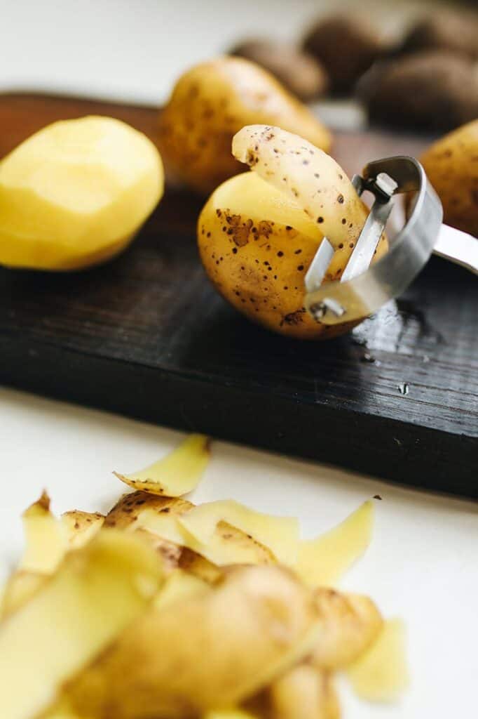 A vegetable peeler cutting through a potato skin, sitting on a cutting board in this guide to the best vegetable peelers.