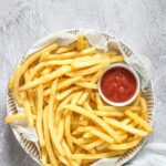 Air Fryer Frozen French Fries on a platter with a small bowl of ketchup nestled between them.