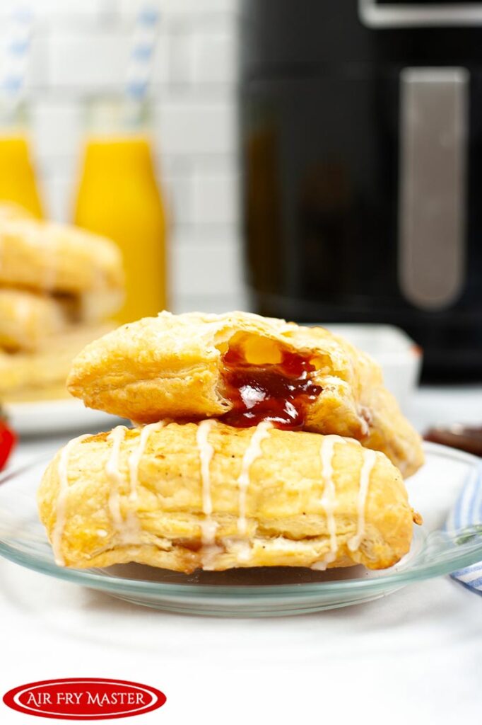 Two Air Fryer Toaster Strudels sit, one on top of the other, which some strawberry jam coming from the corner of the top pastry.