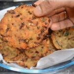 Air Fryer Maddur Vada on a platter. A man's hand holds one towards the camera.