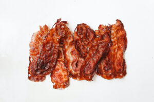 Cooked air fryer pork bacon on a white background.