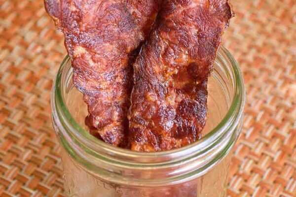 A canning jar sits on a table with three slices of air fryer bacon.