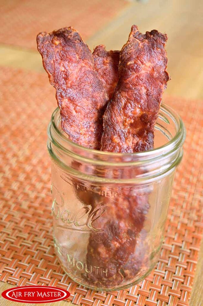Three slices of air fryer bacon sit upright in an open canning jar.