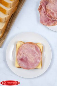 A single slice of bread with cheese and ham on it, resting on a plate.