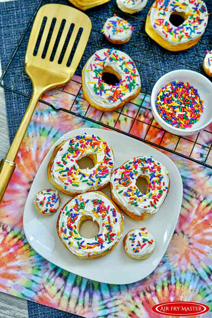 An overhead view looking down at a plate and cooling rack, both filled with this Air Fryer Donuts Recipe With Sprinkles.
