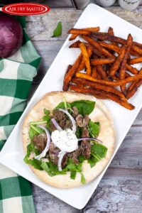 An air fryer steak gyro on a white platter with a side of sweet potato fries next to it.