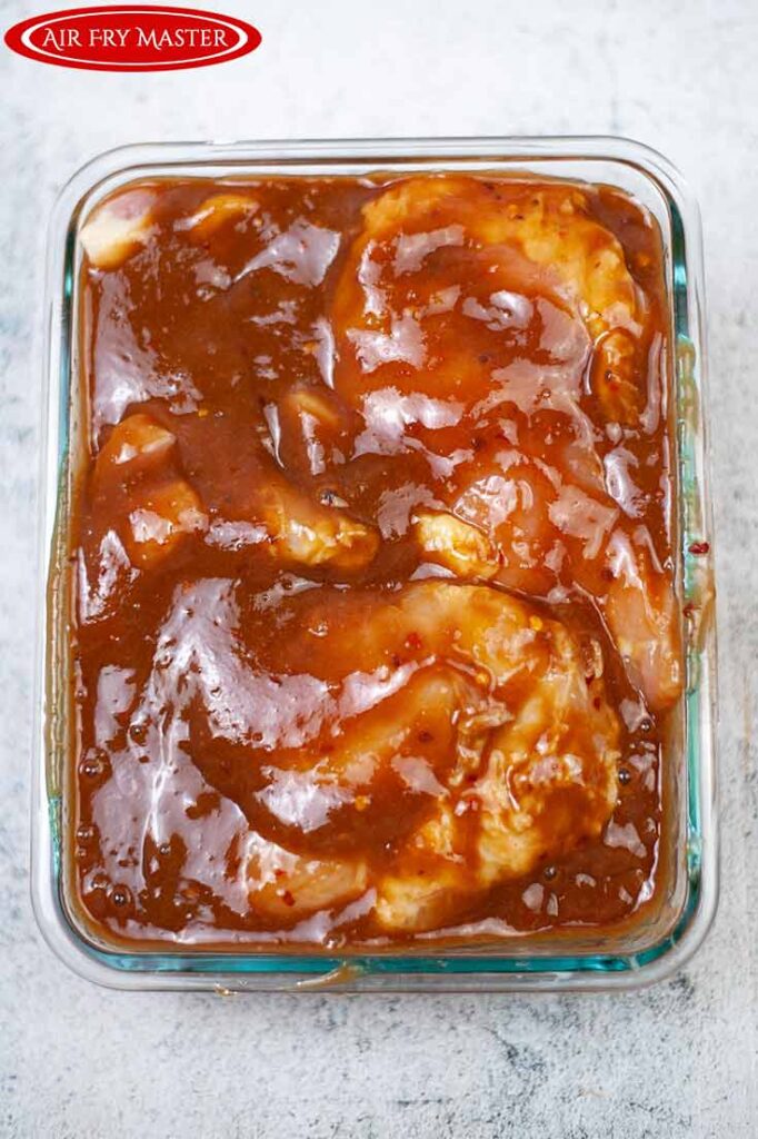 Chicken in a glass casserole dish, marinating in sauce.