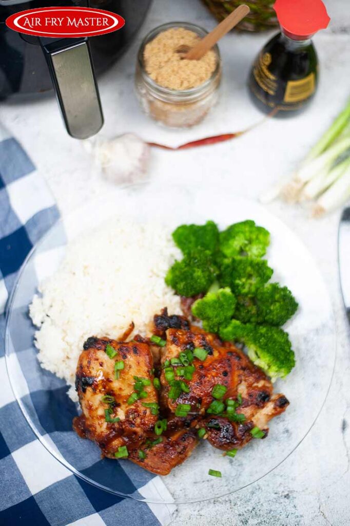 An overhead view of two pieces of Air Fryer Huli Huli Chicken, rice and broccoli sitting on a glass plate.