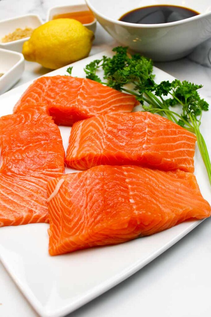 Raw salmon fillets sit on a white platter with the rest of the Air Fryer Honey Glazed Salmon Recipe ingredients sitting behind it.