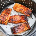 Just cooked Air Fryer Honey Glazed Salmon sits in an air fryer basket on parchment paper.
