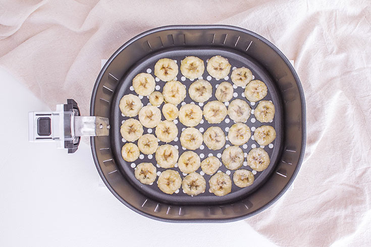 Banana slices sitting in an air fryer basket, waiting to be cooked.