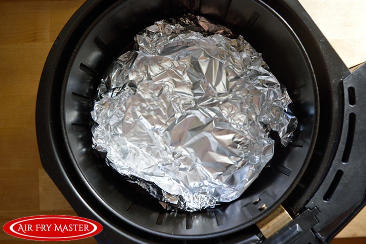 Tin foil lines the inside of a black air fryer basket.