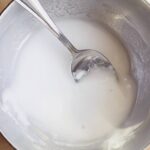 A small metal bowl filled with a baking soda paste. A spoon rests inside the bowl.