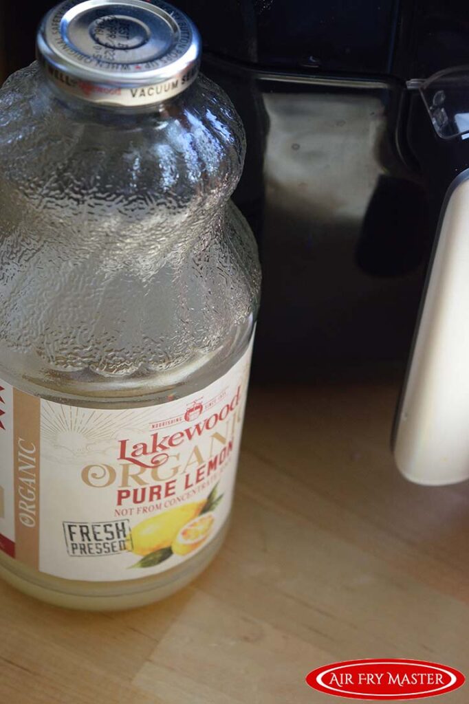 A bottle of lemon juice sits next to a black air fryer.