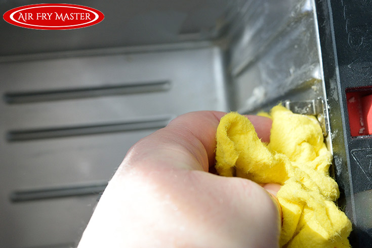 Wiping out the interior of an air fryer with a damp, yellow cloth.