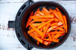 Oiled, cut, raw carrots sitting in an air fryer basket.