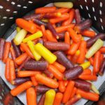 Raw, glazed carrots sitting in a black air fryer basket.