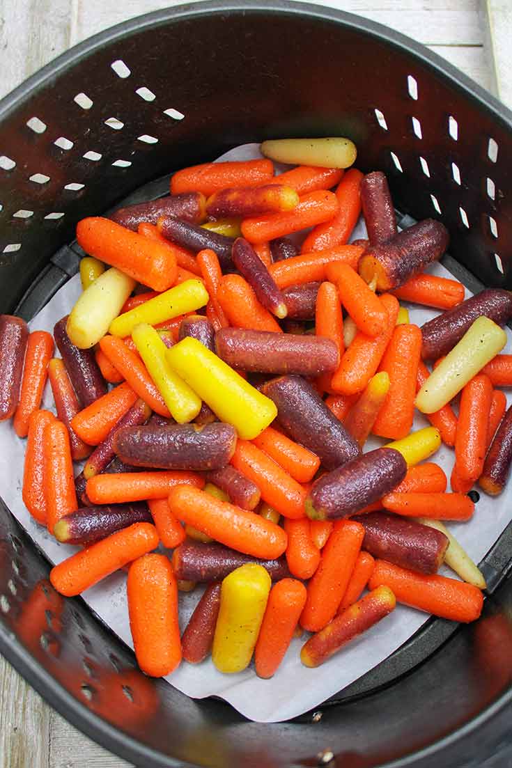Raw, glazed carrots sitting in a black air fryer basket.