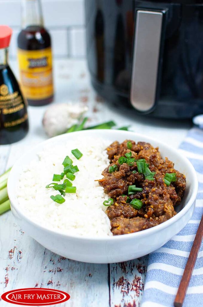 A bowl filled with Air Fryer Orange Beef and white rice and garnished with sliced green onions.
