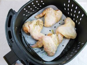 Raw chicken wings sitting in a parchment lined air fryer basket.