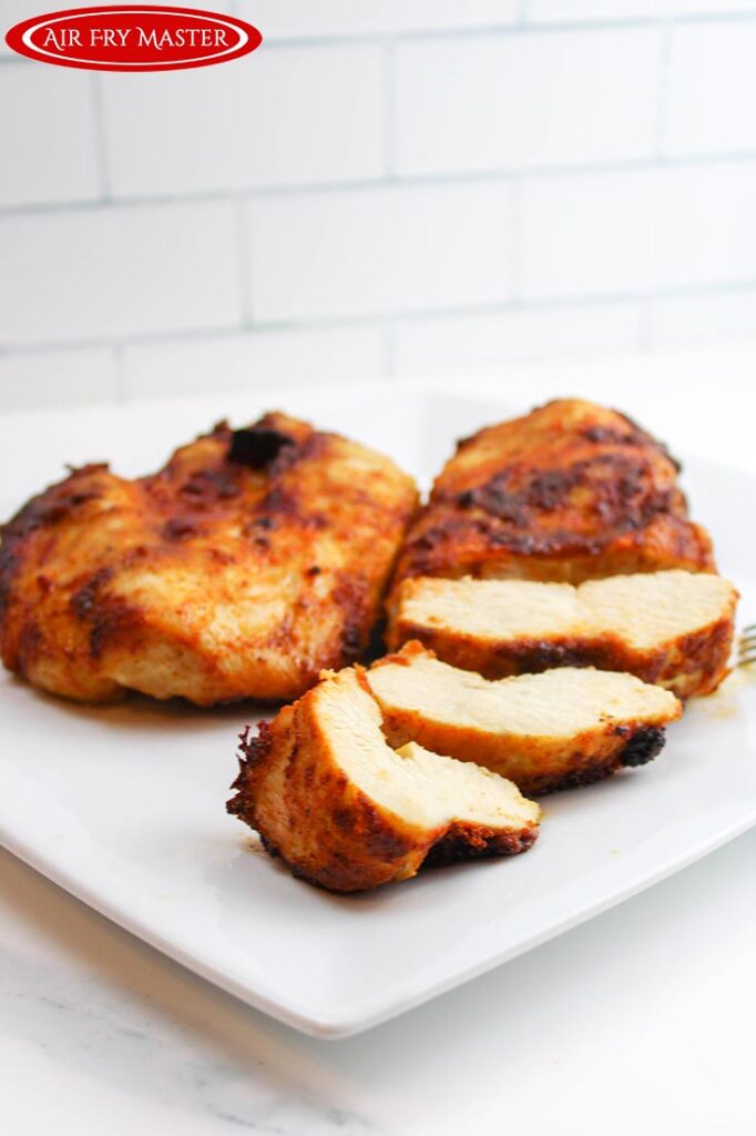 A side view of two chicken breasts on a white plate. One is sliced halfway.