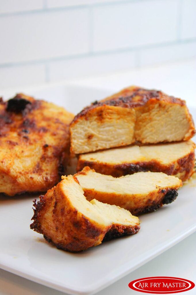 Slices of cooked chicken breast lay on a white plate, ready to eat.