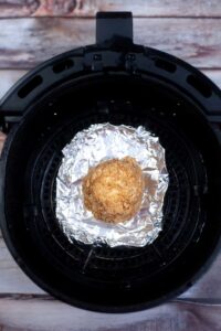 A single ice cream ball sitting a tin foil in an air fryer basket.