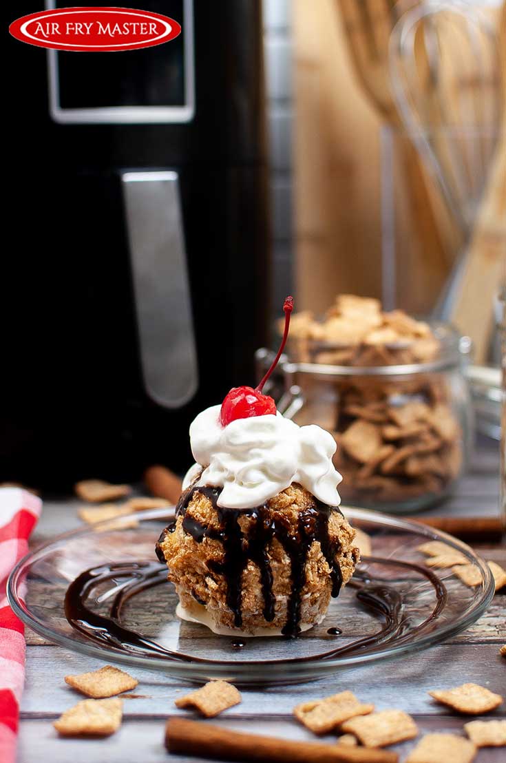 A finished Air Fried Ice Cream ball on a plate, topped with chocolate sauce, whipped cream and a cherry.