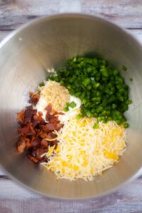 Bacon bits, cheese, garlic and bell peppers in a stainless steel mixing bowl. All are chopped or grated.