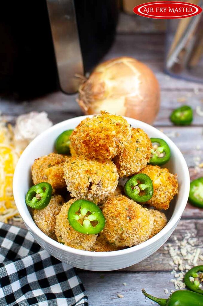 A side view of a white bowl filled with Air Fryer Jalapeño Popper Bites and garnished with slices of jalapeno peppers.