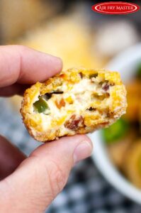 A hand holds a single Air Fryer Jalapeño Popper Bite towards the camera. A bite has been taken to show the cheesy insides.