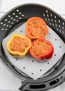 A red, orange and yellow pepper, stuffed with meat and sitting together in a parchment-lined air fryer basket.