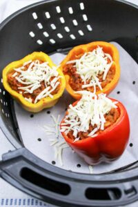 The peppers in the air fryer basket topped with grated mozzarella.