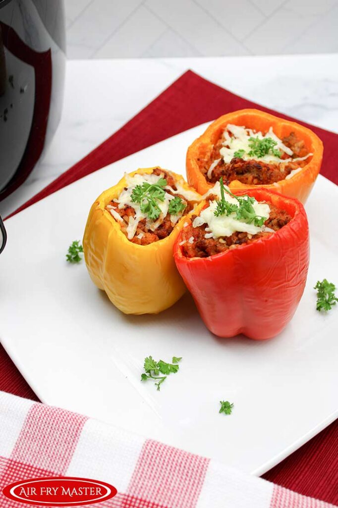 Three stuffed peppers placed on a square, white platter and garnished with fresh parsley.