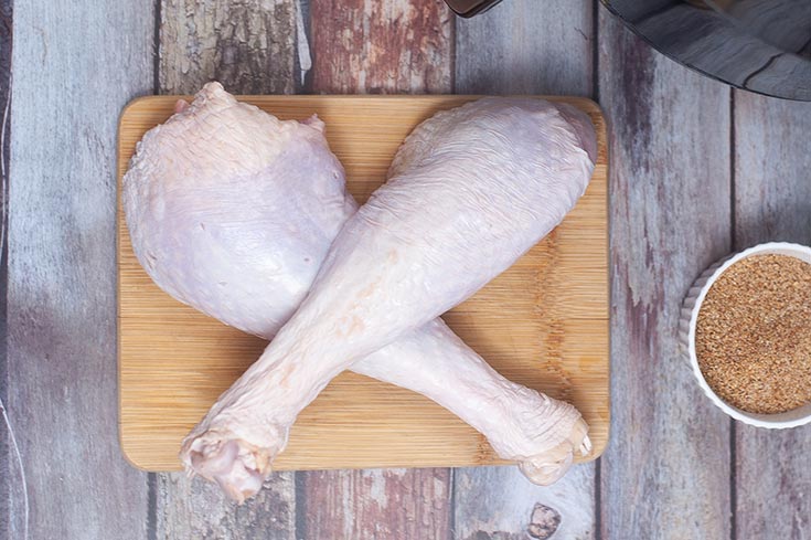 Two raw turkey legs crossed on a cutting board.