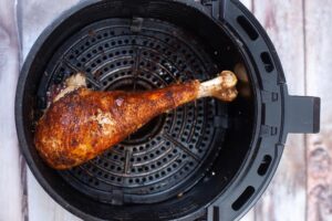 A just-cooked turkey leg sits cooling in an air fryer basket.